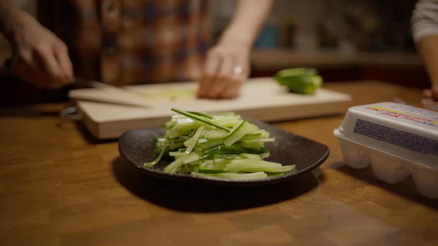 Closeup of a mans hands placing sliced cucumbers with a knife on a plate