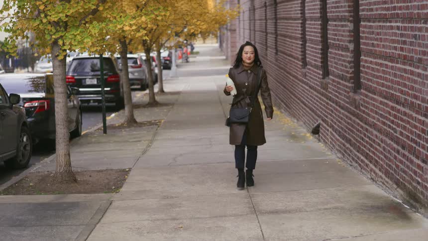 A woman walking through a neighborhood with a bottle of milk in her hand