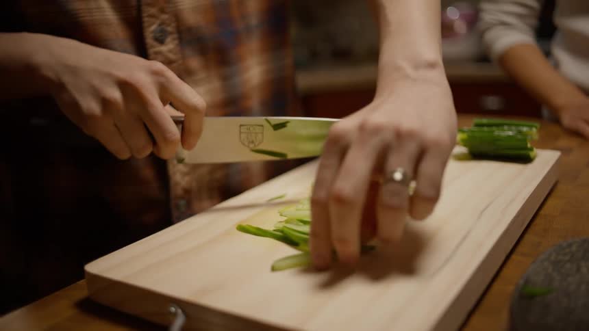 Man slicing cucumber and handing a piece to his girlfriend