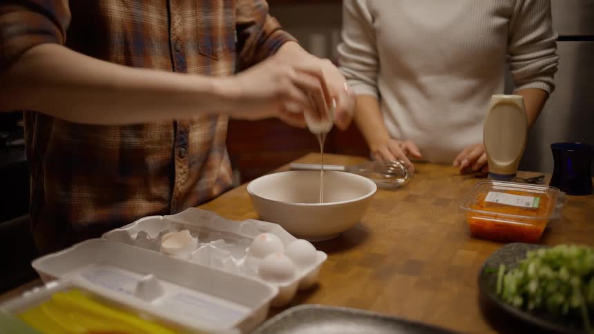 Two people stand at counter cracking eggs into a bowl