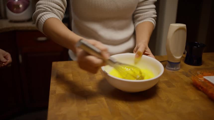 Man and woman beating egg in a bowl on the kitchen counter
