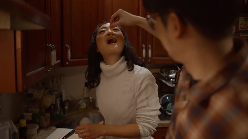 Man feeds woman food while cooking in the kitchen at night