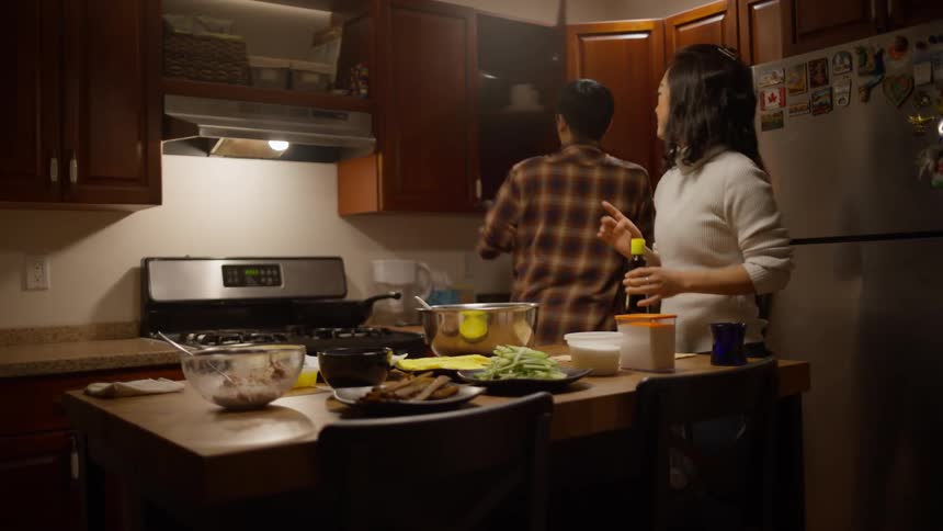 A man prepares a meal while a woman watches him