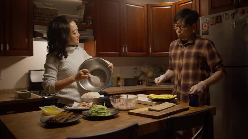 An asian man and woman plate and prepare a large meal in the kitchen