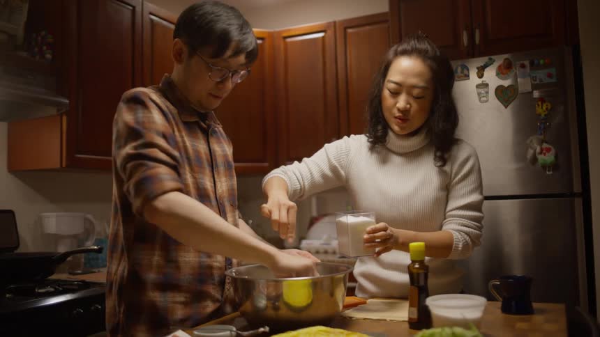 A man and a woman cooking in a large metal bowl on the kitchen counter