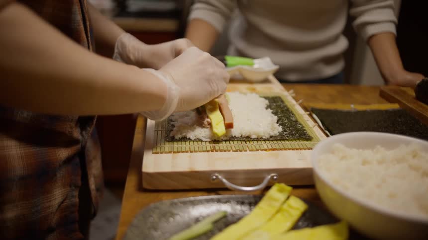 Closeup of a mans hands preparing sushi with another person beside him