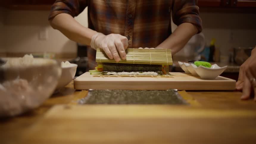 A person carefully prepares a sushi roll in their home kitchen