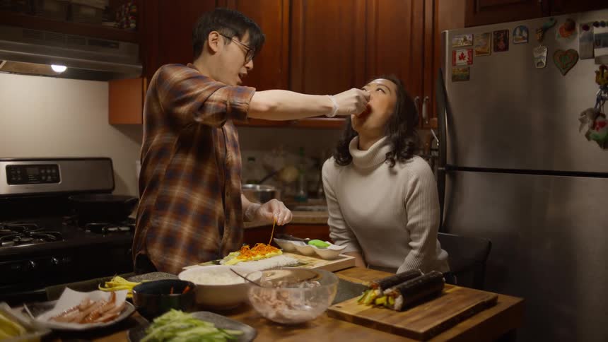 A man prepares dinner while the woman tastes the ingredients