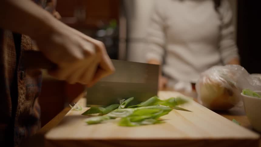 A person using a cleaver to chop vegetables on a wooden board