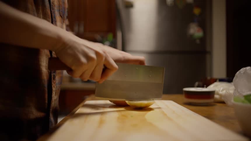Man chopping an onion on a wooden cutting board in the kitchen