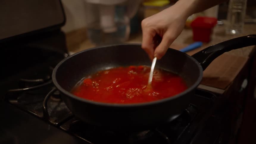 A person mixing a red sauce in a pan on the stove