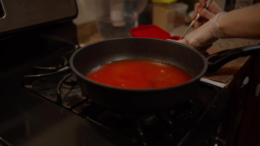 Female cooking at stove adds paste to skillet
