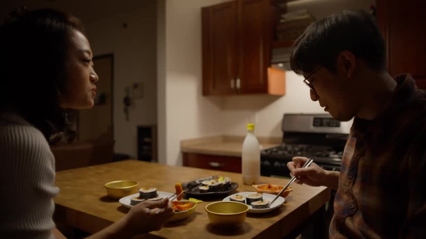 A man and a woman eat sushi at home with chopsticks