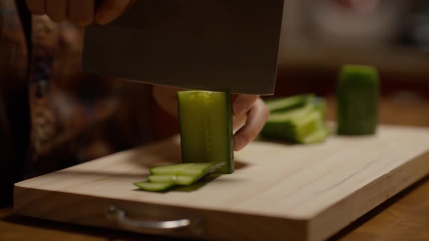Person cutting a cucumber on a wooden cutting board in the kitchen