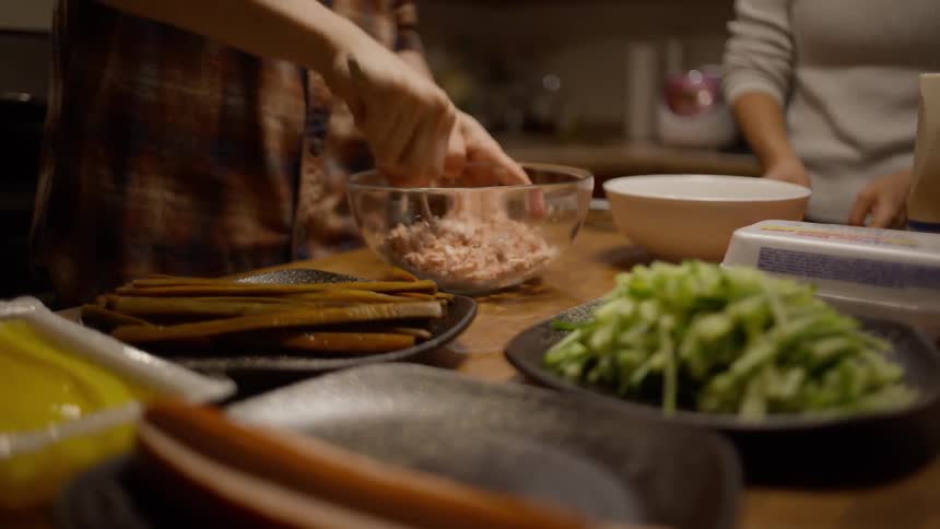 Closeup of two peoples hands cooking at a table while mashing tuna