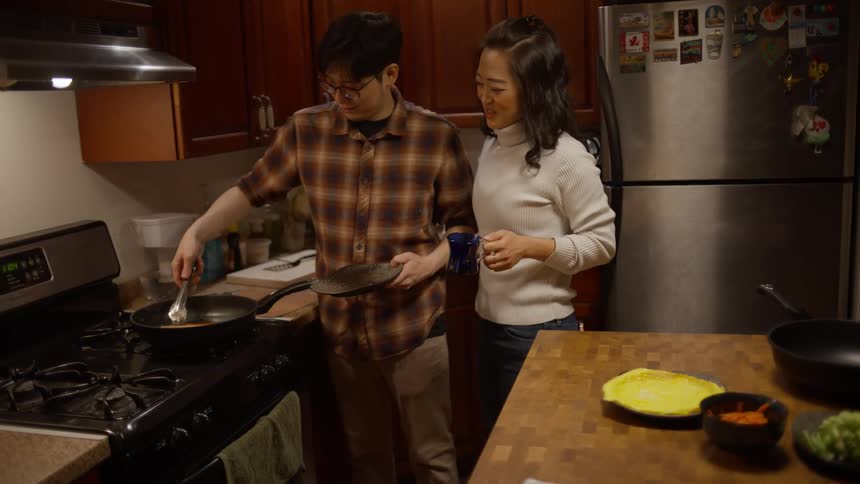 Man and woman in the kitchen chatting and cooking in the frying pan on the stove