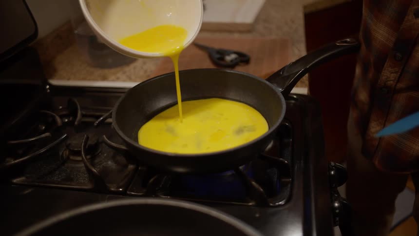 Someone cooking scrambled eggs in a frying pan on the stove