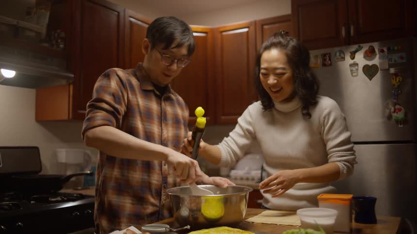 A man and a woman are mixing ingredients in a bowl in the kitchen