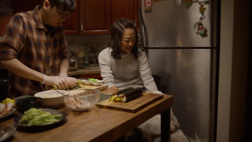 Couple in the kitchen preparing Korean food with the dog beside them receiving affection