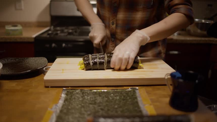 A man cutting fish inside the kitchen while a lady put down a plate on the countertop