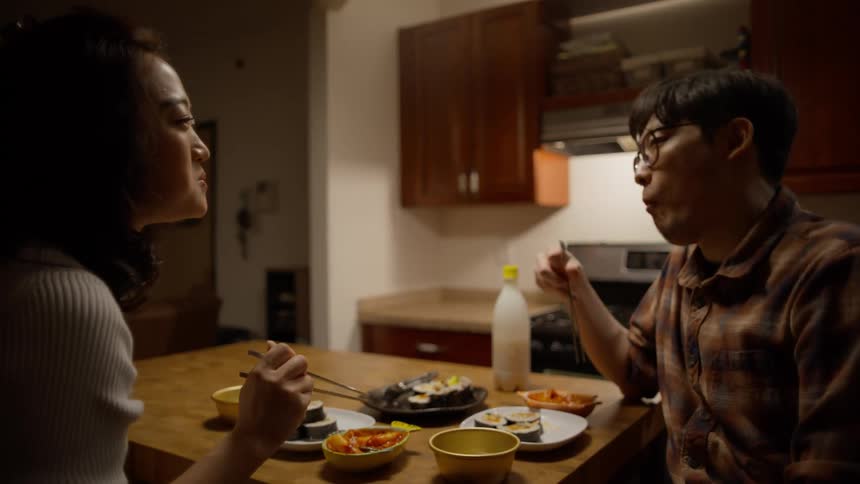 Couple sitting at a table eating food with chopsticks
