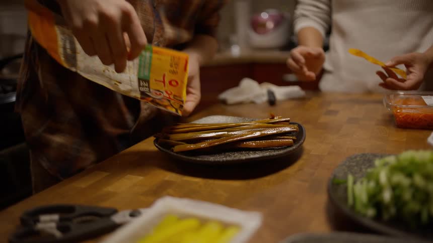 Two people in a kitchen preparing food and serving asparagus on a plate