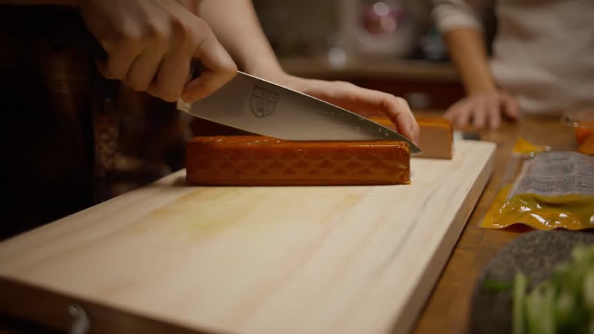 Closeup of a persons hands cooking and cutting a protein with a knife