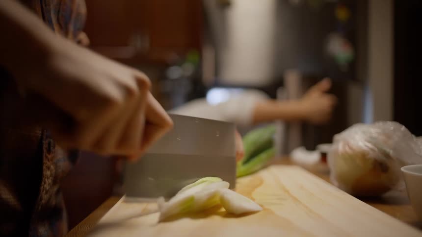 Closeup of a man chopping vegetables and a woman searching in the refrigerator