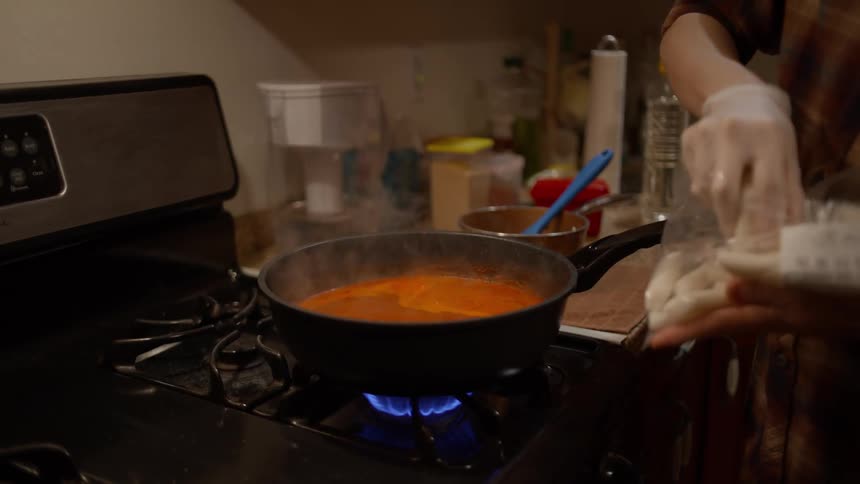 A person wearing latex gloves cooking at home