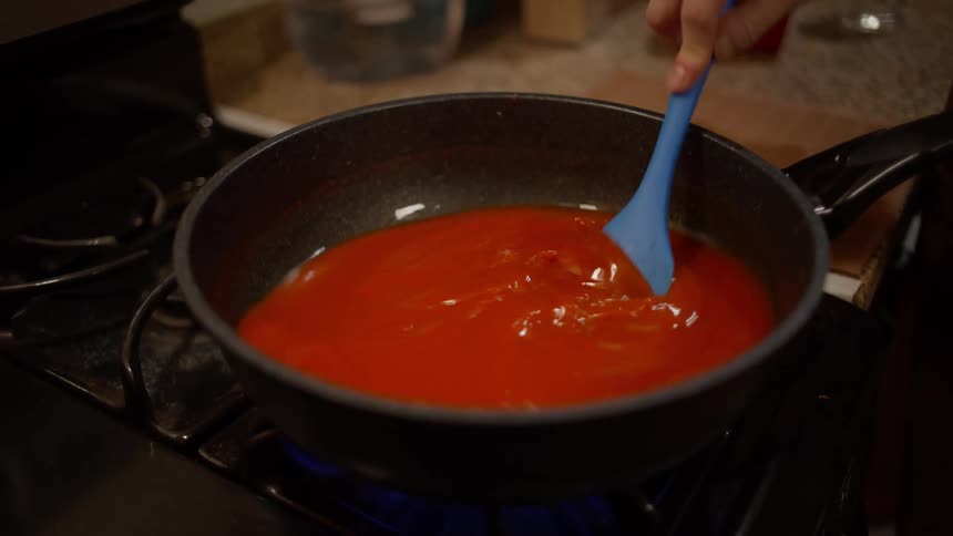 A person stirring red liquid on a stovetop in a home kitchen