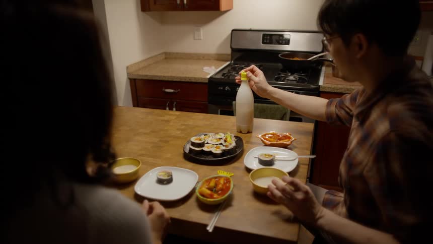 Couple sitting at the table with Korean food serving themselves and drinking from a bowl