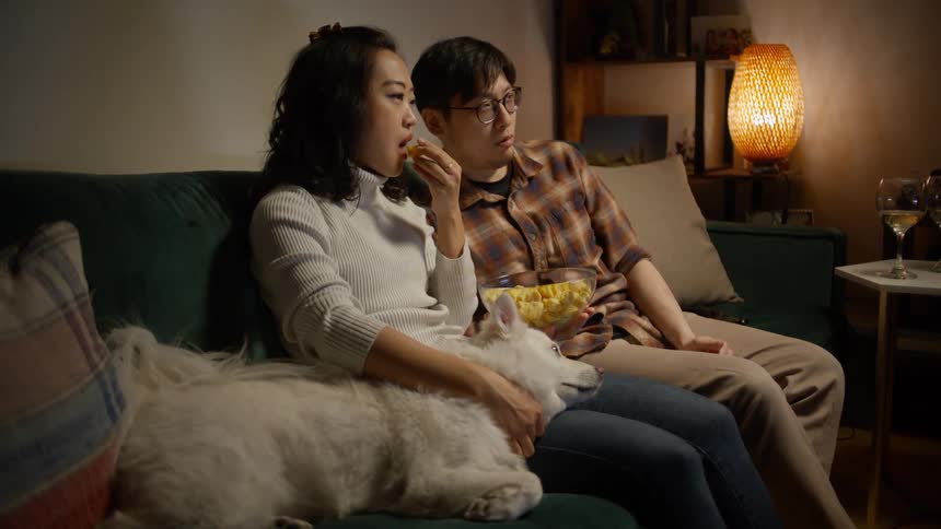 Couple sitting on the sofa with their dog eating popcorn