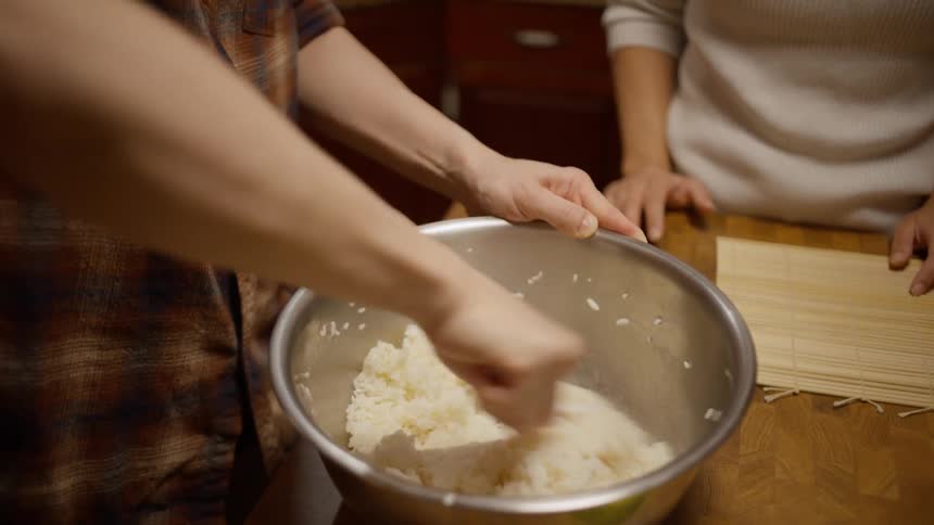 Closeup of a persons hands preparing cooked rice in a pan