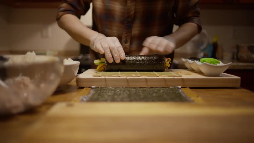 Closeup of a mans hands with gloves preparing sushi