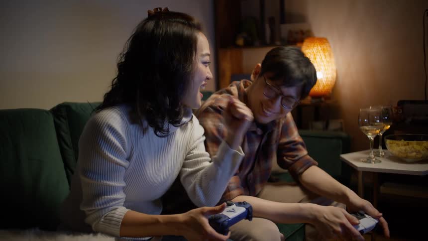Couple sitting on the couch holding a game controller playing and the woman cheering