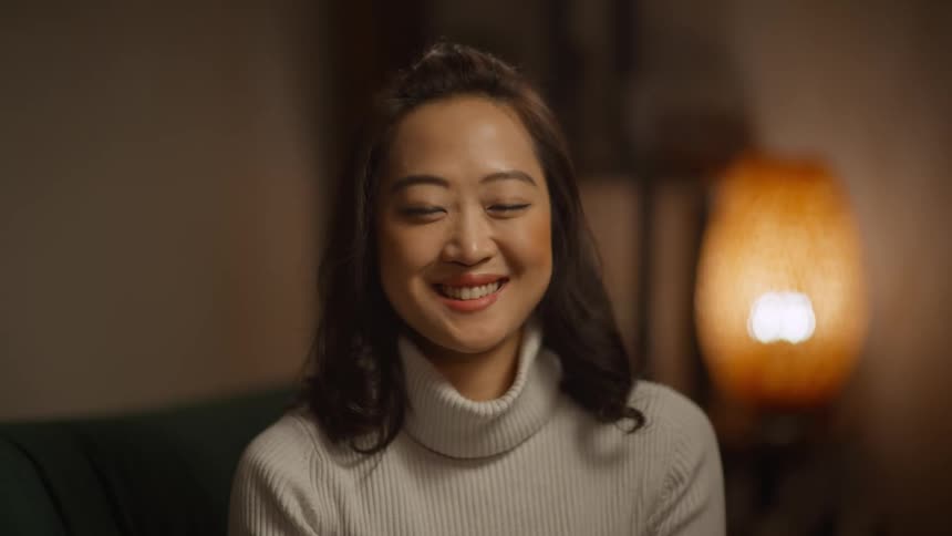 Close up of woman wearing a white turtleneck sweater smiling sitting on the couch in the living room