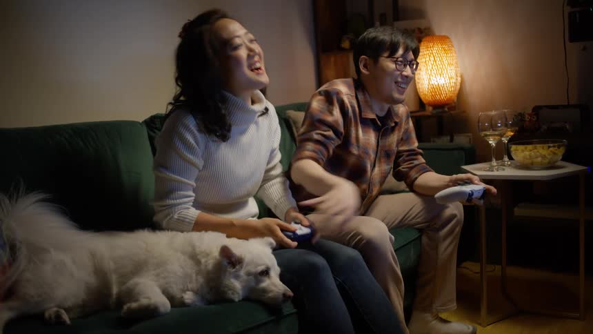 Man and woman sitting on the couch with their dog playing video games and having fun together