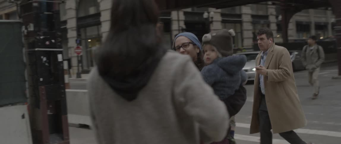 A woman holding a baby crosses a busy city street and is approached