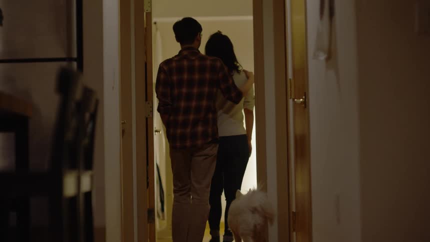 Couple walking towards the bedroom in the house with the dog right behind