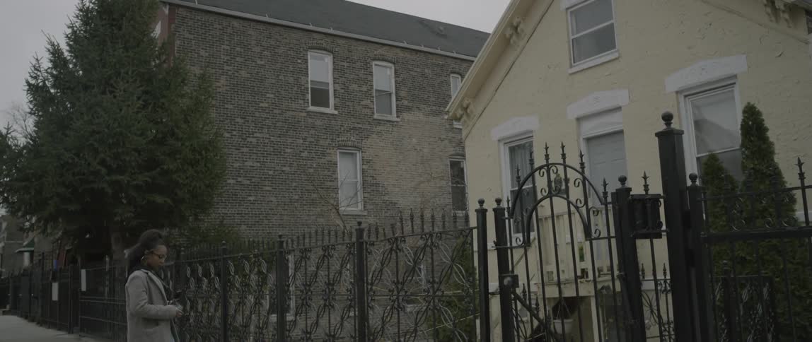 A woman walks past an iron fence in front of a home