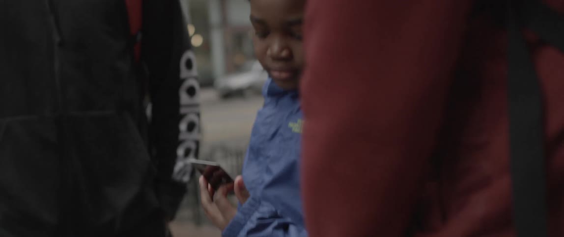 A boy looks at a phone and talks to people