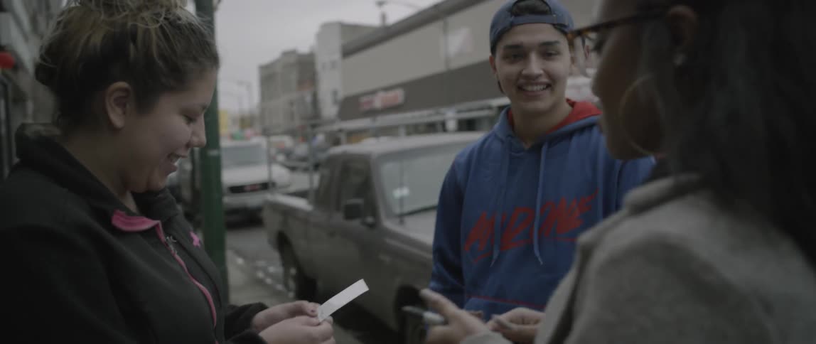 Woman gives a man and woman a polaroid picture on a city sidewalk