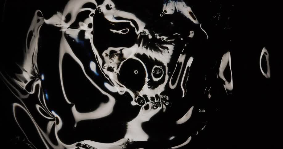 Light reflects on a black viscous oil like substance as it moves rippling out from the center