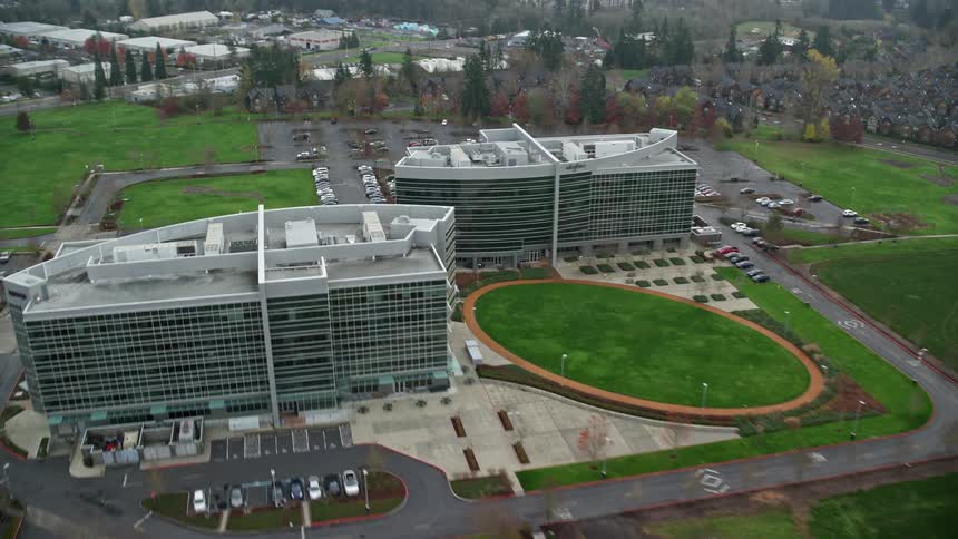 Two office buildings and behind a large parking lot full of cars