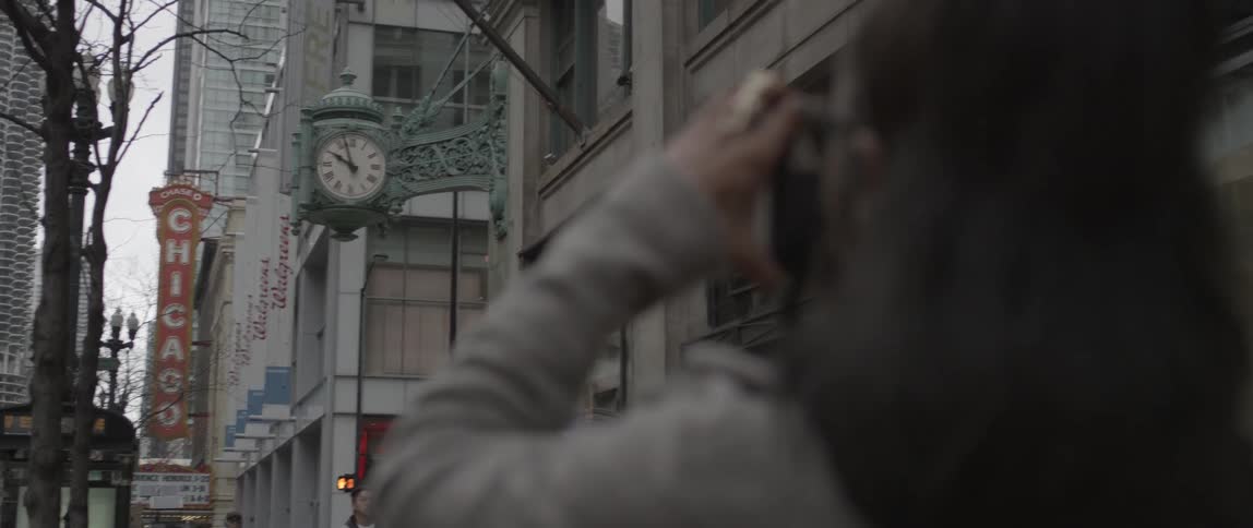 A woman takes a picture of a clock on a building