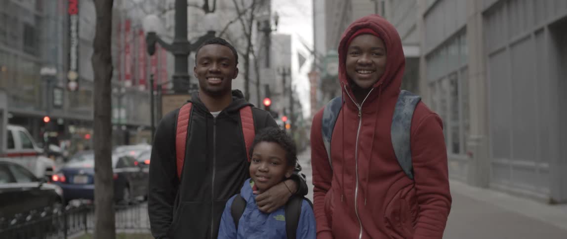 Three boys laugh and smile on a city sidewalk