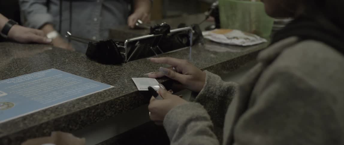 A woman writes on a photograph and hands it to a store teller