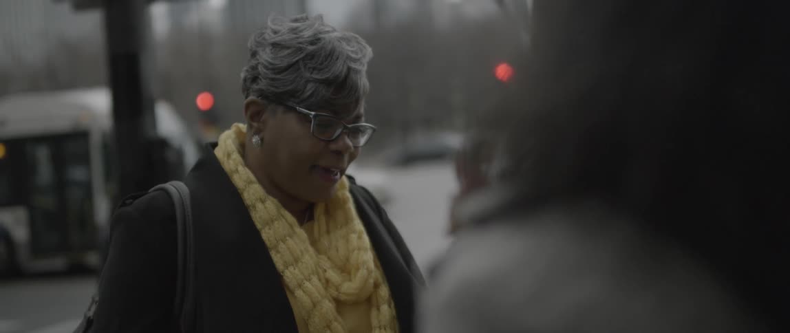 A woman gives a polaroid picture to another woman on a city street
