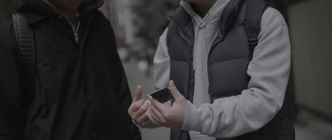 Two guys look at a phone on a city street