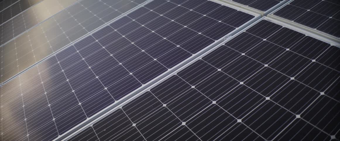 A row of solar panels black solar panels with 12x6 grids with a row above tilted with sunlight reflecting